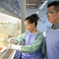 Two scientists in lab coats and goggles working in a lab.